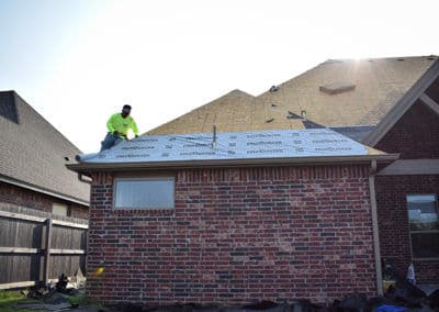 Worker installing a new roof on a brick house under sunny skies.