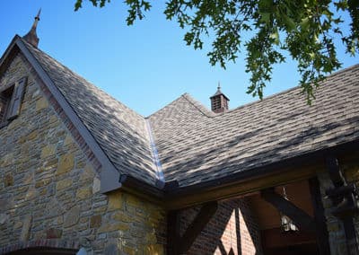 Stone house roof with shingles under a clear blue sky, featuring decorative gables.