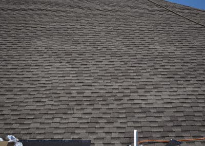 Close-up of a textured asphalt shingle roof with a clear blue sky in the background.