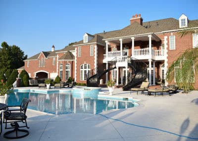 Luxurious brick mansion with a spacious pool and elegant outdoor seating area.