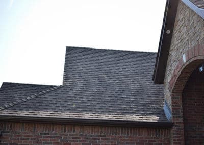 Residential roof with shingles and stone accents against a clear sky.