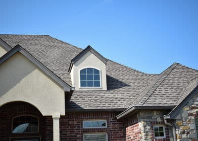 Residential house exterior with a gable roof and stone accents against a clear blue sky.