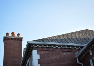 Brick house chimney and roof against a clear blue sky.