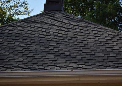 Gray asphalt shingles on a residential roof with trees in the background.