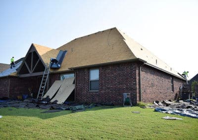 Roof replacement in progress on a brick house with workers and ladder visible.