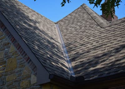 Slate roof shingles on a house with a stone exterior and clear blue sky background.