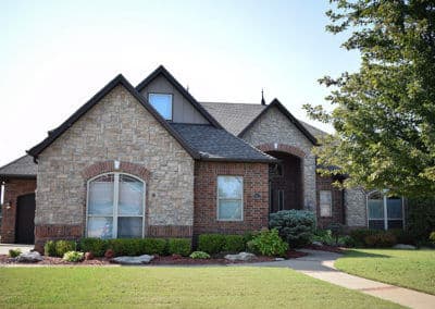 Single-story brick and stone house with a landscaped yard and clear blue sky.