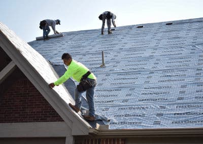 Workers installing a new roof with protective covering on a residential building.