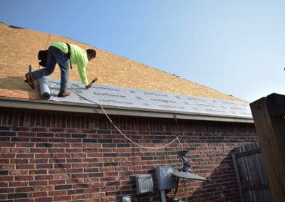 Worker installing roofing underlayment on a residential house, showcasing construction activity.