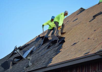 Workers installing shingles on a roof under clear blue sky, demonstrating roofing techniques.