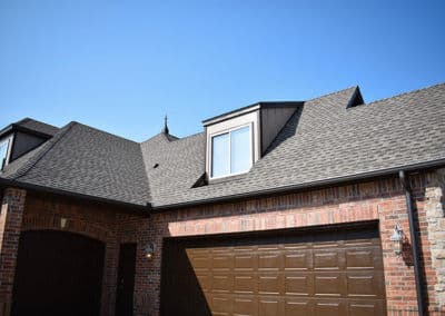 Brown brick house with a dark shingle roof and garage under clear blue sky.