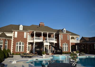Luxurious mansion with outdoor pool, patio, and elegant architecture against a clear sky.