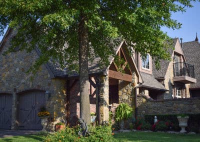 Beautiful stone house with lush landscaping and a large tree in sunny outdoor setting.