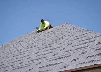 Worker installing roofing material on a sloped roof under a clear blue sky.
