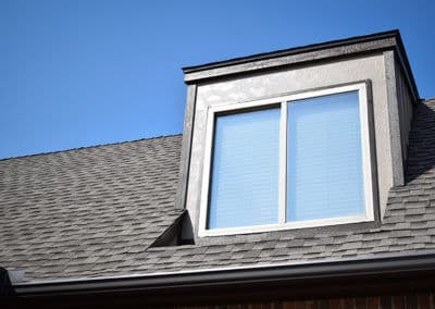 Attic window on a sloped roof with clear blue sky in the background.