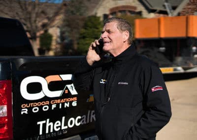 Man in jacket talking on phone next to a roofing truck, showcasing outdoor roofing services.