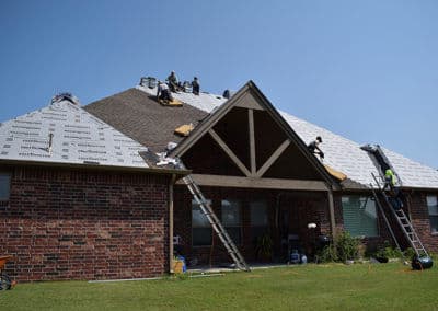Roofing crew installing new shingles on a residential home under clear blue skies.