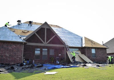Roofing crew installing new shingles on a residential home under clear blue skies.