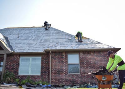 Roofers installing shingles on a residential home under a clear blue sky.