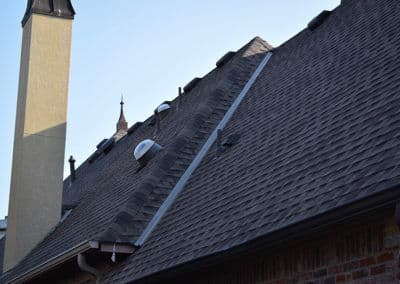 Roof with asphalt shingles, chimney, and ventilation pipes against a clear sky.