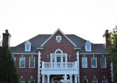 Elegant brick mansion with white columns and balcony under a clear sky.
