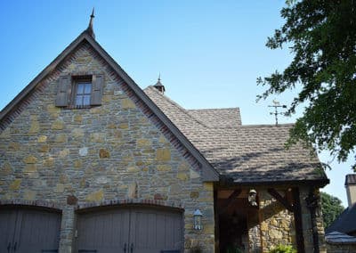 Stone house exterior with peaked roofs and wooden garage doors under a clear blue sky.