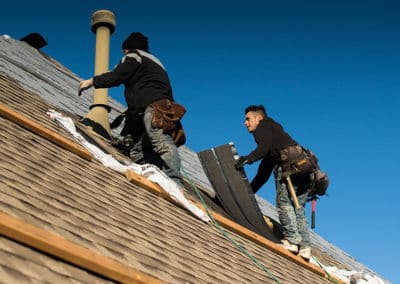 Roofers installing shingles on a residential roof against a clear blue sky.