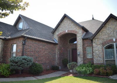 Front view of a charming brick and stone house with landscaped garden and trees.