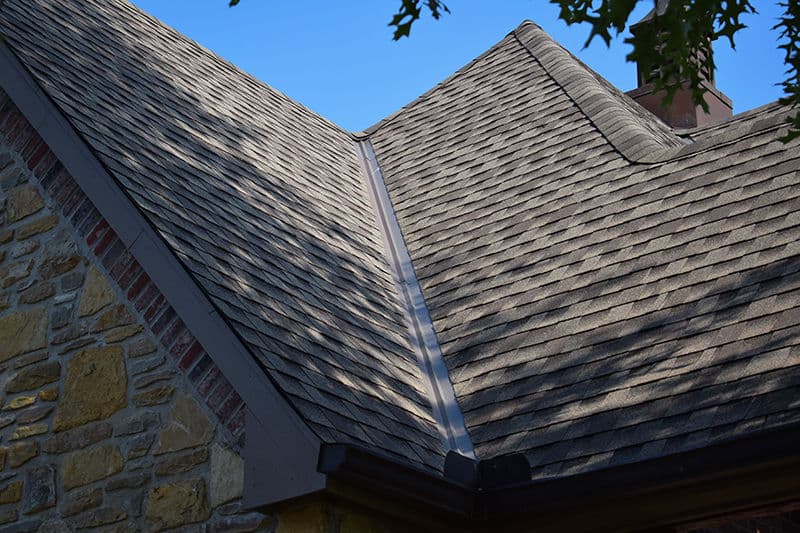 View of a sloped roof with shingle tiles and drainage gutter against a blue sky.