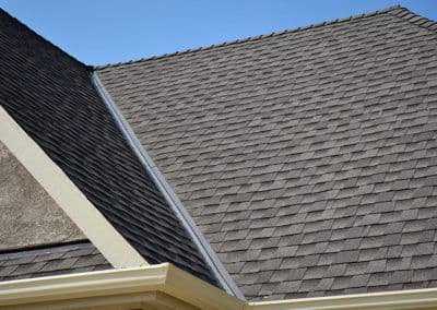 Close-up of a gray shingle roof with a clear blue sky in the background.