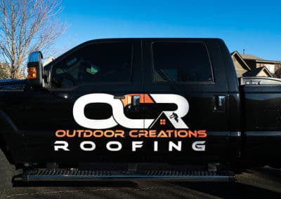 Black truck featuring "OCR Outdoor Creations Roofing" logo, parked in residential area.