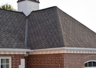 Close-up of a residential roof with gray shingles and a brick wall exterior.